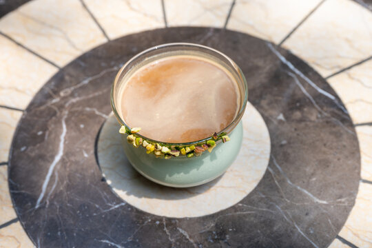 A cup of frothy coffee sits on a marble surface, surrounded by intricate patterns.