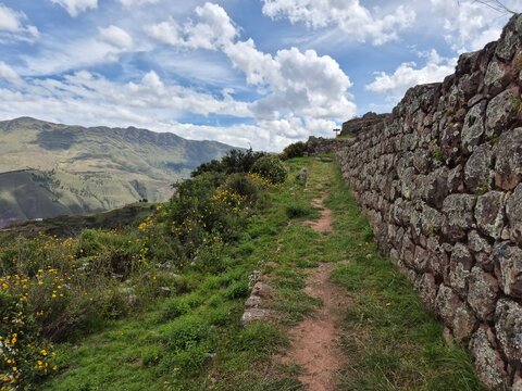 Grassy hiking path with stone wall and scenic mountain valley view