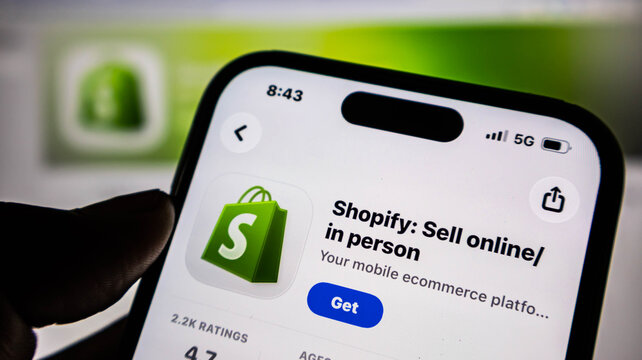 Closeup of a hand holding a smartphone displaying the shopify mobile app store page for ecommerce business management and online selling