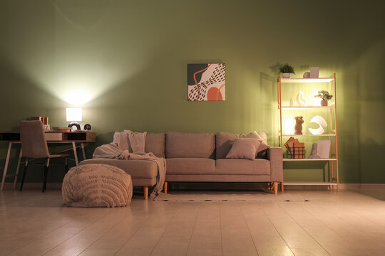 Interior of stylish living room with grey sofa, glowing lamps and coffee table at evening