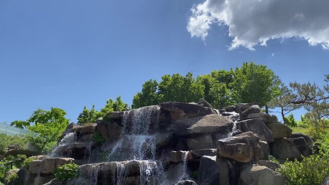 Beautiful artificial waterfall cascading down rocks under a bright blue sky