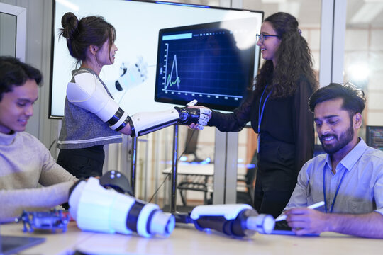 A breakthrough in human augmentation. A female engineer tests the haptic feedback of a bio-integrated prosthetic, shaking hands with the user in a research lab.