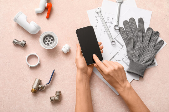 Female hands with blank mobile phone, set of plumber's items and house plans on pink grunge background