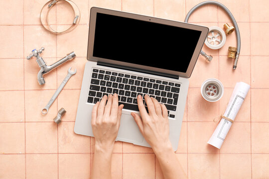 Female hands with laptop, set of plumber's items and house plant on beige tiled background