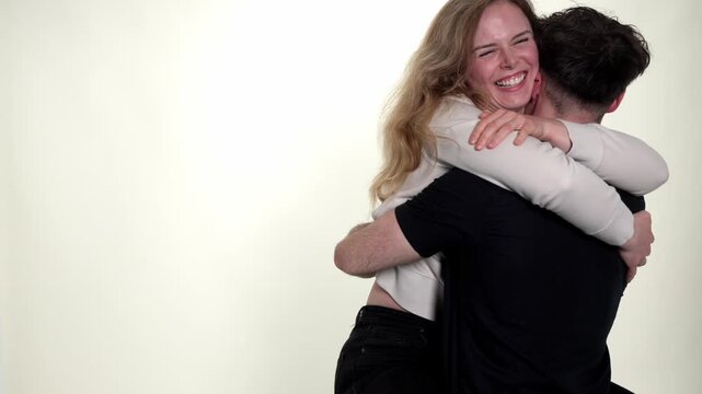A young couple embraces with evident love and affection, showcasing happiness and connection. The man and woman hug each other in slow motion against a clean white studio background, conveying intimac