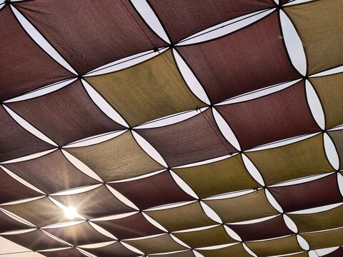 Sunlight filters through a patterned canopy of alternating brown and green fabric squares