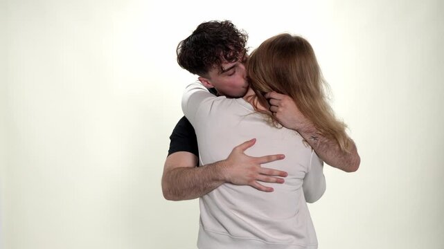 A young couple is captured in a tender embrace, with the man hugging the woman from behind against a clean white studio background. It is projects focusing on relationships, emotional well being, and 