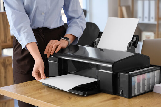 Young businesswoman using printer on table in office, closeup