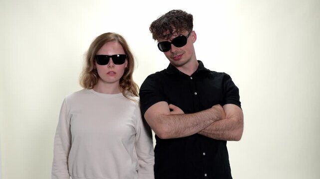 A cool couple poses confidently with sunglasses in a studio setting, embodying concepts of fun, love, and modern style. The man and woman stand together against a clean white background, showcasing th