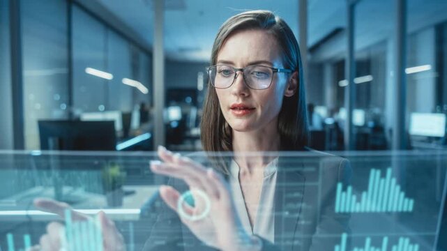 Focused businesswoman using futuristic digital touchscreen in modern office with data charts and graphs