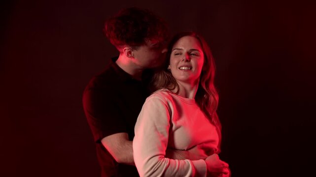 A romantic couple shares an intimate moment, embracing closely under a dramatic red light. The man gently kisses the woman s cheek, highlighting themes of love, affection, and deep connection. This ci