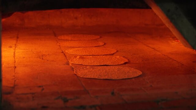 Detailed close up of traditional handmade round Matzot baking in a hot wood-fired stone oven; fast-paced professional process for the Jewish Passover holiday showing flames and texture.