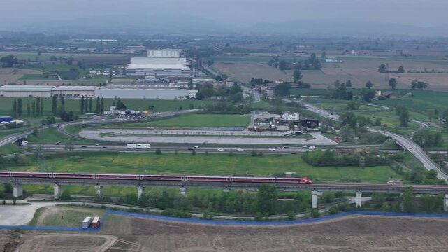 Frecciarossa high speed train on AV high speed line near Fi&igrave;orenzuola D Arda exit, PC Emilia Romagna Italy running parallel to A1 and A21 motorways across Po Valley farmland, drone tracking shot