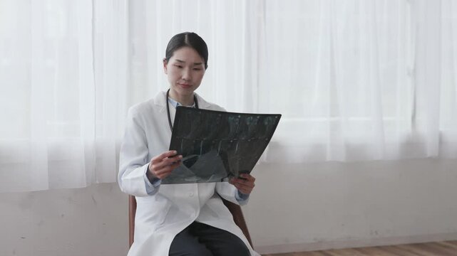 Asian Female Doctor in White Coat Reviewing X-ray Image