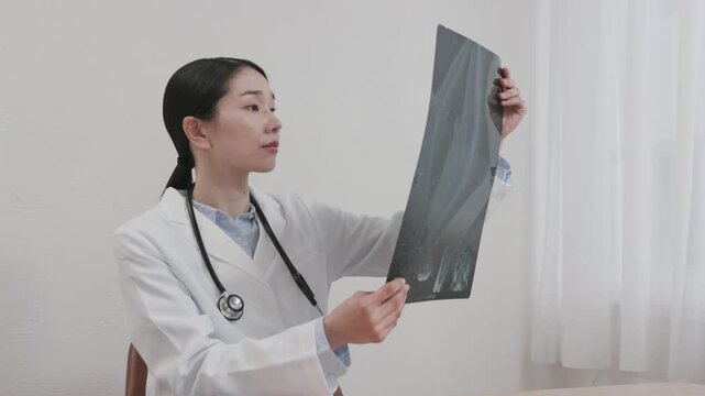 Asian Female Doctor in White Coat Reviewing X-ray Image