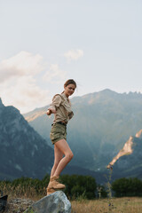 Fototapeta premium Vibrant woman enjoying the outdoors in a mountain landscape, smiling with relaxed posture, sunlit breeze, casual outfit, natural colors, scenic terrain, carefree mood