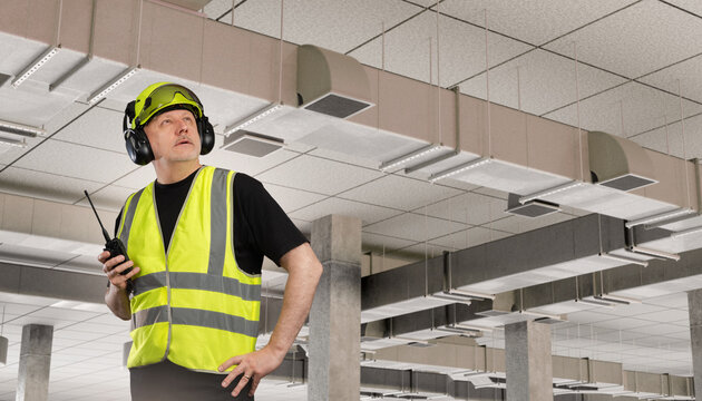 HVAC inspector checks suspended ventilation ducts during indoor building systems inspection.