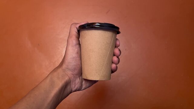 Male or men hand holding paper cup of take away drinking coffee. orange floor on the background. front, side. top view, high angle, above, flat lay. bright. isolated.