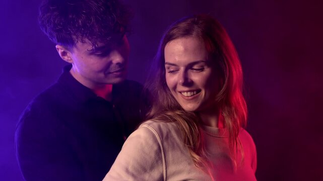 A young couple is captured in a moment of love and fun, embracing each other with genuine smiles. The scene is illuminated by vibrant green and red lighting, creating a dynamic and romantic atmosphere