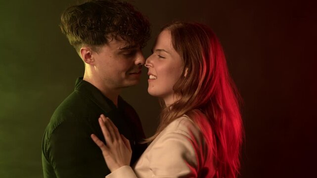 Love and intimacy concept a young couple embracing closely with their faces near each other, illuminated by vibrant red and blue neon lighting. The man and woman share a tender, passionate moment, con
