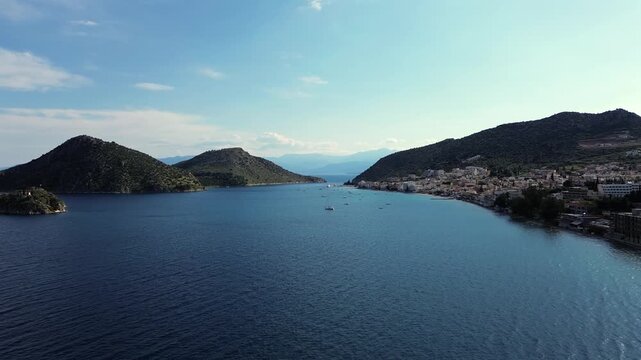 Beautiful 4K drone panorama over the protected Tolo bay and scenic Romvi island. Revealing a coastal tourist resort town, calm blue sea waters and small boats anchored in summer.