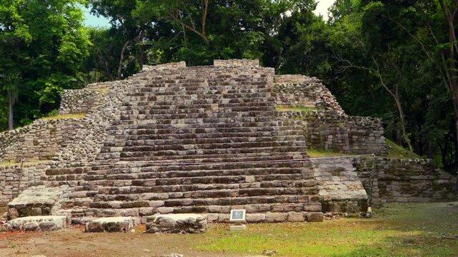 Ancient Mayan pyramid structure and central altar at the historical Oxtankah Archaeological Zone surrounded by lush trees.