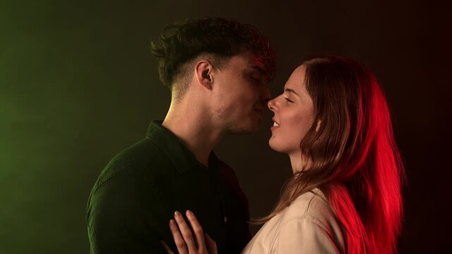 Love and connection concept a young couple embracing and kissing in a studio setting. The scene is illuminated with contrasting red and green lights, creating a moody and intimate atmosphere. This foo