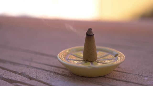 Cone shaped citronella incense stick smoking gently in a ceramic holder on a stone ledge