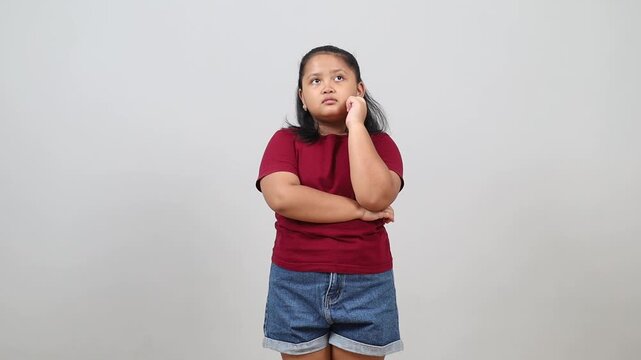 Pleased thoughtful Asian little girl is raising-up his finger while coming up with an idea standing isolated over white background
