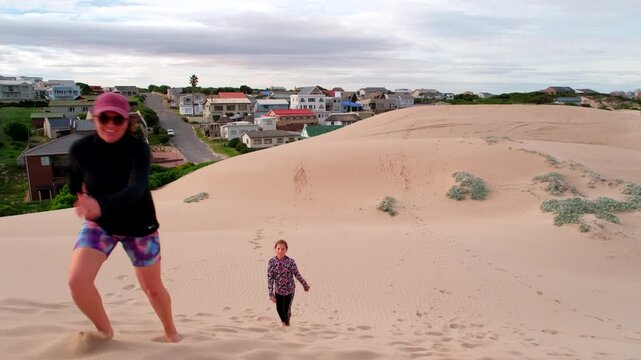Funny top view of active mom racing daughter laboriously up sandy dune