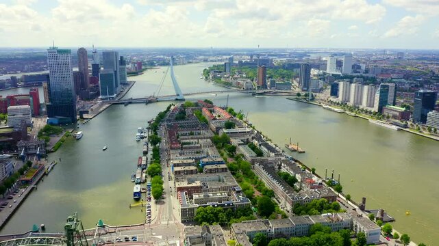 Rotterdam, Netherlands. Erasmus Bridge, its 139-metre steel pylon and 40 stay cables spanning the Nieuwe Maas, Drone footage over Noordereiland with the city skyline beyond. Drone footage