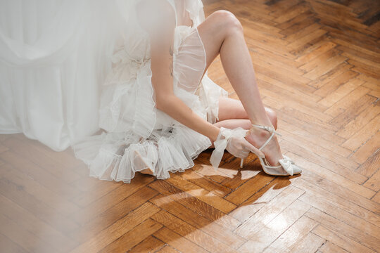 Fashionable woman in a short ruffled bridal dress sitting on a vintage wooden parquet floor.