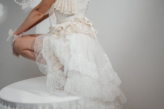 Bold woman in a creative bridal dress sitting on a decorated white table, showcasing lace details and high heels.