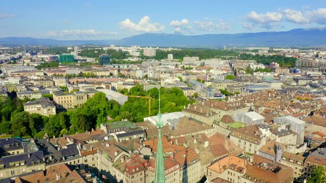 Geneva, Switzerland. St. Pierre Cathedral, its slender green copper spire and mismatched towers rising above the terracotta rooftops of the Old Town, Drone footage under a bright summer sky. Drone fo