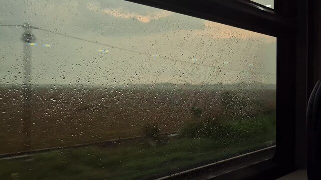 Raindrops on a moving train window looking out at the green rural landscape during a rainy day journey