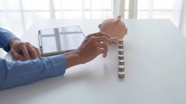 Asian Businessman holding pen counting stacking coin with piggy bank.