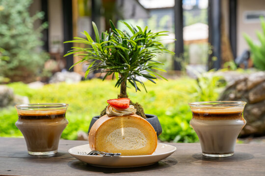 A beautifully arranged table features a slice of bread with a cherry tomato on top, flanked by two glasses of latte. The setting is outdoors, with lush greenery and a serene garden in the background