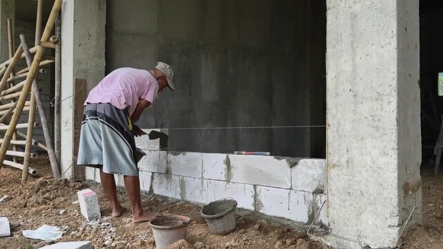 Detailed footage of a construction worker performing masonry work by pouring liquid cement mortar onto a hebel (AAC) block before carefully placing the next block on top