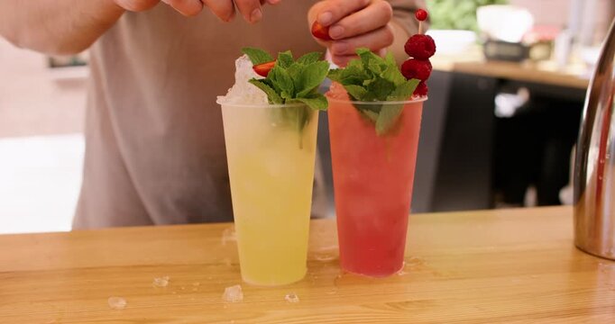 Garnishing cocktails. Refreshing beverages. Unrecognizable barman hand using mint leaves raspberries with crushed ice at bar counter.