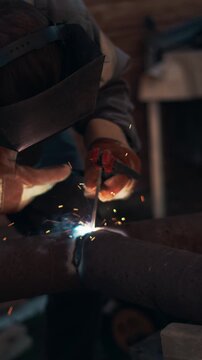 Industrial worker welding large metal pipe outdoors with bright sparks and smoke. Professional craftsman wearing protective gloves and mask during heavy steel fabrication process.