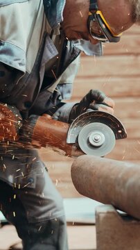 Home craftsman cuts thick metal pipe with electric grinder in outdoor workshop beside country house. Industrial sparks and protective gloves show safe DIY work and reliable repair solutions.