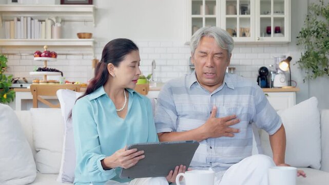 Senior Asian man suffers from heartache. Man has heart attack, seizure sitting on couch at home. Unwell old male chest pain myocardial infarction, chronic cardiology disease