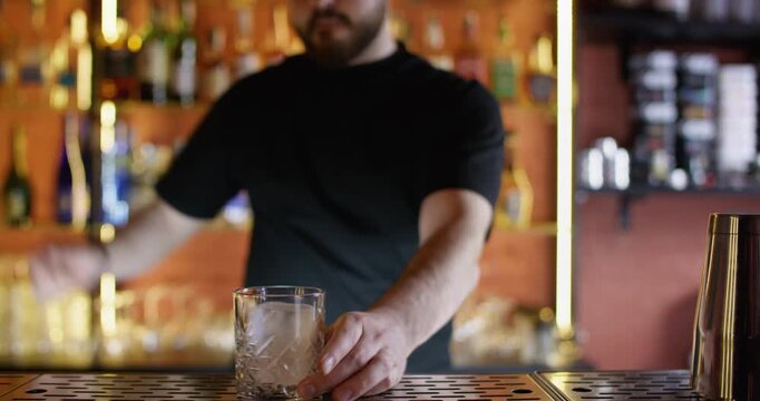 Ice glass. Cocktail making. Professional male bartender using cold cube rocks preparing refreshing alcohol drink in bar.