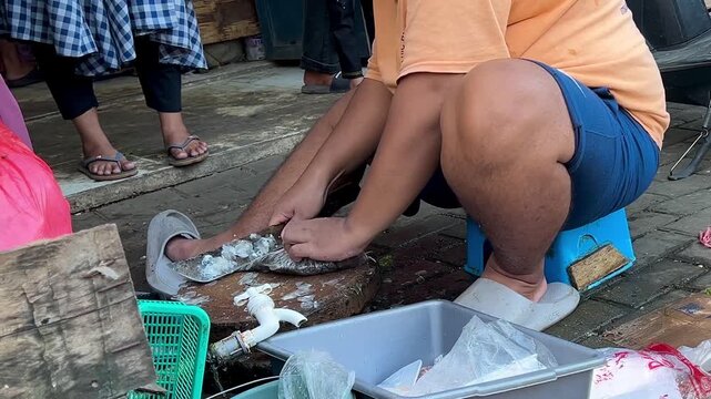 A fish seller cleaning fish scales before selling the fresh fish at a market.