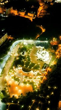 Vertical video. Gelendzhik, Russia. Cathedral of St. Andrew the First-Called, snow-white walls and golden domes, the night, Drone footage over Andreevsky park with light trails from traffic on the M4