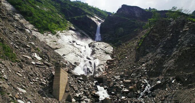 A powerful waterfall cascades down a rocky landslide gully surrounded by green slopes in the Himalayas of Nepal.