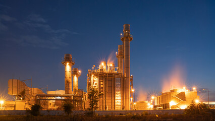 Industrial Powerhouse at Dusk: A massive power generation facility, illuminated by artificial lights against the twilight sky, stands as a symbol of industrial might and energy production. © Rassarin