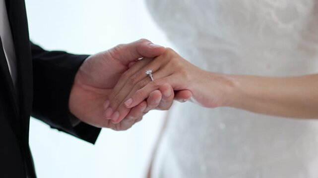 Close up of bride and groom holding hands with engagement ring during wedding ceremony.