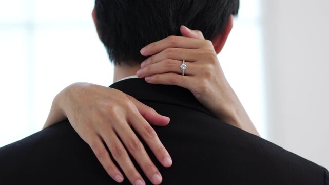 Close up of bride embracing groom while showing engagement ring during wedding ceremony.