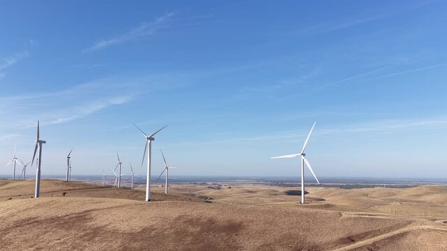 Panoramic drone footage flying over the arid hills of the Altamont Pass Wind Farm in California, showcasing numerous spinning wind turbines producing clean and sustainable alternative energy
